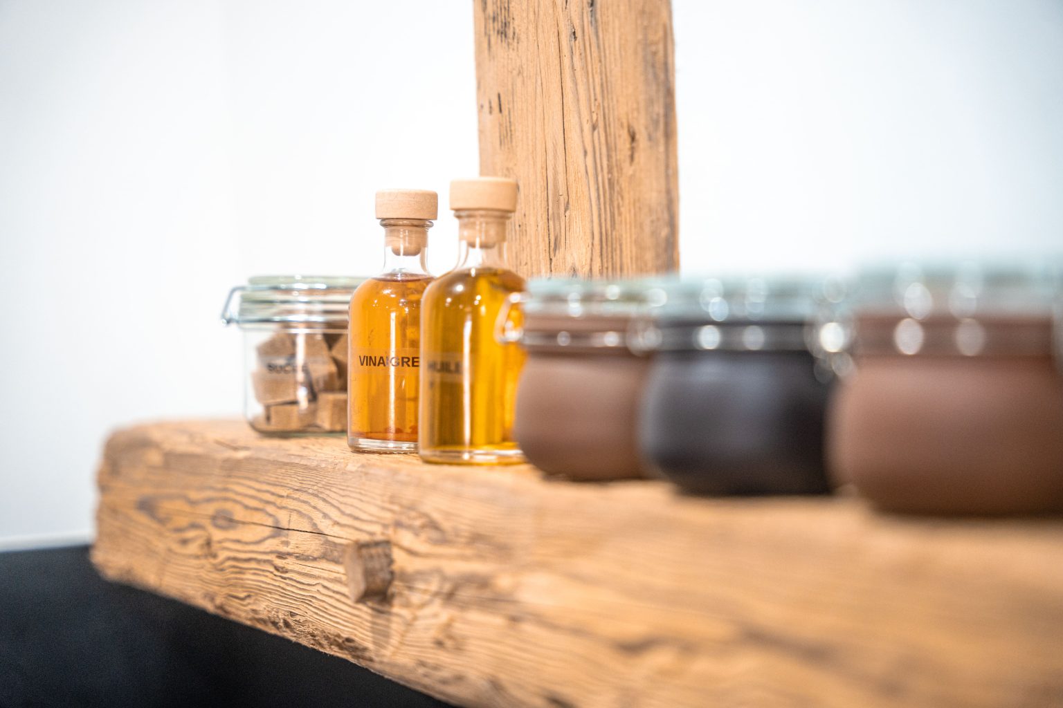 Plusieurs bocaux en verre et flacons de condiments, tisane, thé, joliment disposés sur une étagère en bois dans la cuisine du Gîte du Clos de l'Orme à SAINT ANTOINE dans le DOUBS